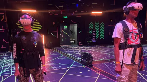 Two men in virtual reality headsets and jackets on a dancefloor