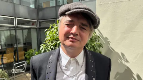 BBC Singer Pete Doherty. He is wearing a tweed cap and back blazer with studded lapels
