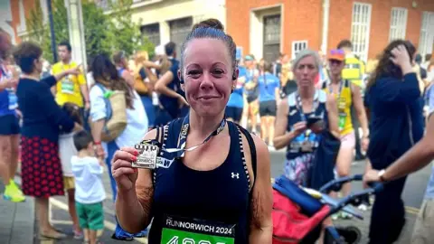 Lucy Hughes having completed Run Norwich smiling at the camera and holding her medal