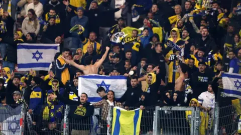 Reuters Maccabi Tel Aviv fans at a football game chanting and holding up a variety of flags and scarves.
