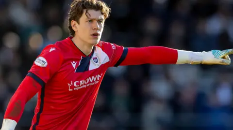 Jon McCracken, wearing a red goalkeeper's jersey, points during a game for Dundee in the 2025-26 season