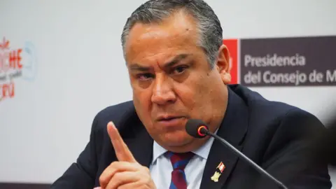 Carlos Garcia Granthon/Fotoholica Press/LightRocket via Getty Images Gustavo Adrianzen gesticulates during a news conference in November 2024. He is wearing a dark suit with a pin with the Peruvian flag on his lapel. 