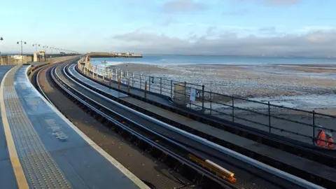 TomW A frosty train platform which runs off towards the sea with a beach at the side of it.