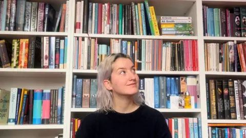 A woman with platinum blonde hair in front of books