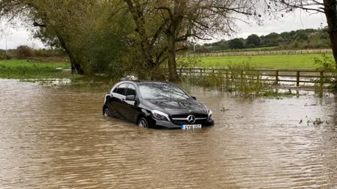 Car flooded in water with trees and field in background