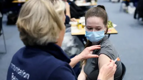 Reuters A nurse administering a vaccine to a woman sat in a black chair next to her.