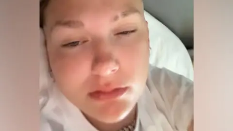 A selfie of a young woman lying in a hospital bed