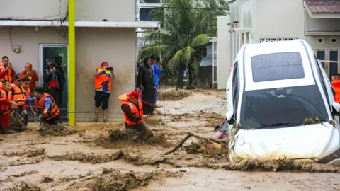Rescuers attempt to pull a car from rapidly moving floodwaters in Indonesia
