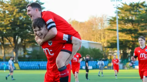 FC Isle of Man Two football players celebrating a goal, with one carrying the other on his back