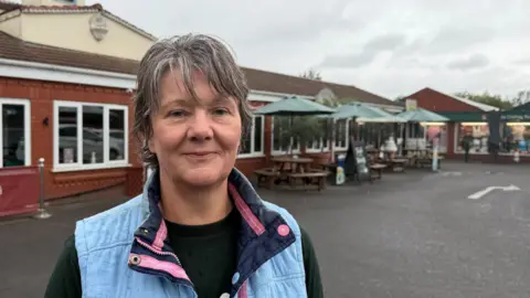 A middle-aged woman with grey hair looks at the camera