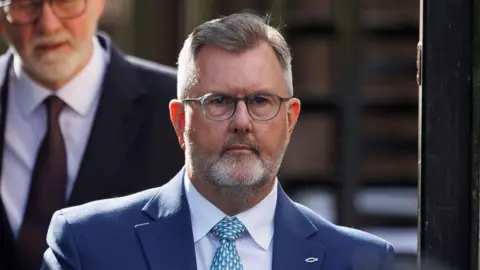 PA Media Sir Jeffrey Donaldson, pictured from the shoulders up, wearing a dark blue suit, light blue shirt and spotty blue tie. He has a tight grey beard and grey hair and is wearing glasses. 