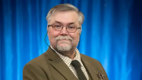 Festival of Sheppey A man with glasses, grey hair and a beard smiles at the camera 