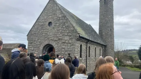 Crowd of people queuing outside the entrance of a stone church 