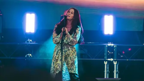 Blenheim Palace Festival Alanis Morissette performing at Blenheim Palace. She is holding the mic stand whilst singing into it.