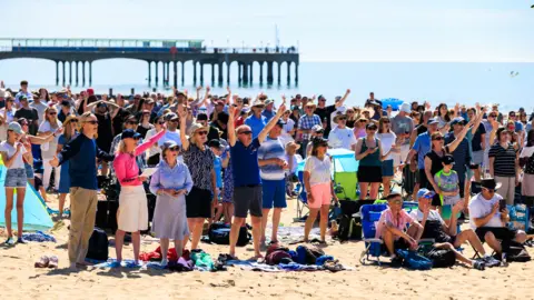 BCP Church Collective Hundreds of people stand on Bournemouth beach with Boscombe pier in the background
