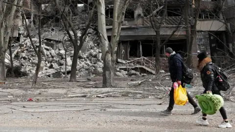 Reuters Local residents walk past an apartment building destroyed during Ukraine-Russia conflict in the besieged southern port city of Mariupol, Ukraine March 31, 2022