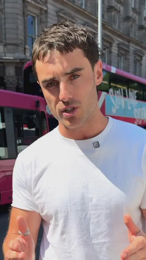 A man in a white shirt standing in front of a pink bus