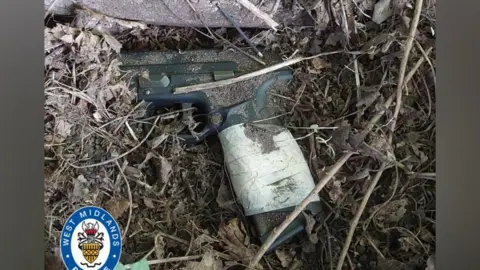 West Midlands Police A photograph of a gun that has been dumped surrounded by twigs, leaves and dirt