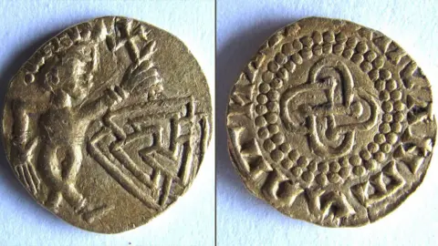 Adrian Marsden A composite image showing two sides of a 7th Century gold coin. On the left, the side depicts a male figure, with crossed legs, a diadem/headdress, holding up a cross in its left hand above an interlocking design of three triangles. On the right it depicts abstract designs with a cross-like shape in the middle, enclosed by a double row of dots, enclosed by a meaningless jumble of Latin-style characters. 