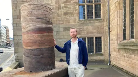 Mr Stephenson is stood next to the sculpture on the plinth at Liverpool Parish Church