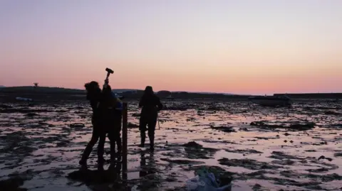ROWAN HENTHORN A picture of scientists holding equipment at sunset on marshland.
