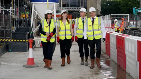 BBC News Rachel Reeves and Angela Rayner are dressed in brown work boots, black trousers, a fluorescent bib with a hard hat, as they tour a construction site