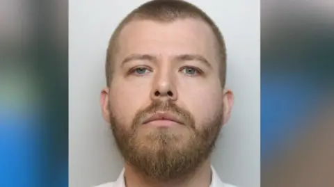 Derbyshire Police Mugshot of a man in a white shirt. He has a buzzcut and a light brown beard.