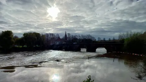 A view of a bridge Warrington, with the sun shining through the cloudy sky and reflecting on the river