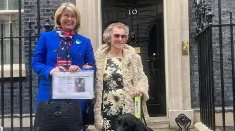 Justin Dealey/BBC Jill Allen-King and former Southend West and Leigh MP Anna Firth. They are standing in front of the black door of Number 10 Downing Street. Allen-King has a black labrador in front of her.