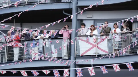 Andrew Matthews/PA People are standing on a balcony which is decked out with red, white and blue bunting.