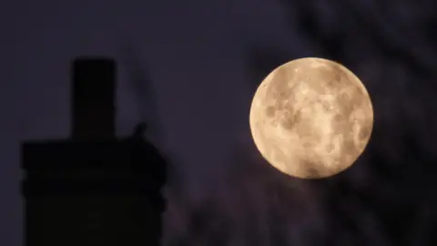 MrBlueSky/WeatherWatchers The moon on the right gives the illusion of being as large as a Chimney framing it on the left. 