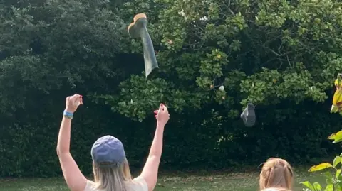 A woman wearing a blue hat throws a wellington
