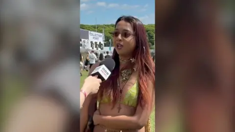 A woman wearing sunglasses and a green bikini top speaks into a BBC News microphone.