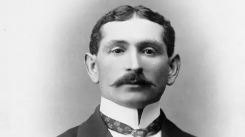 Manchester Jewish Museum Man with smart curtain hair and a upturned collar with tie and suit jacket.