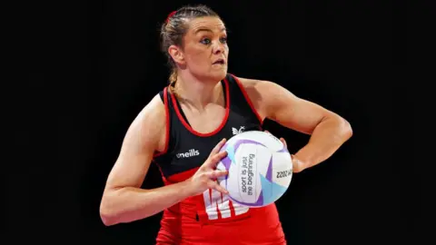 Getty Images Close up of Nia Jones playing netball. She wears a Cardiff dragon netball dress and holds a ball in front of her with both arms. 