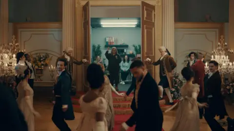 Courtesy of Netflix Actors dance at a Regency-style ball inside the Georgian ballroom as the doors are opened from behind a make-shift office training room. 