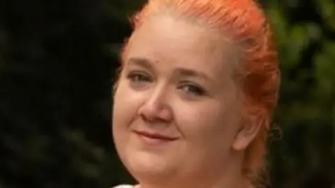 Rhiannon with ginger hair in a plait smiling at the camera