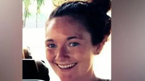 Danielle McLaughlin smiling at the camera. She has long auburn hair tied up in a bun. She is wearing a dark, patterned top.