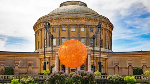 Mike Selby/National Trust The Helios sculpture on display at Ickworth House. It is a large sphere shape and has been lit up in a yellow colour.
