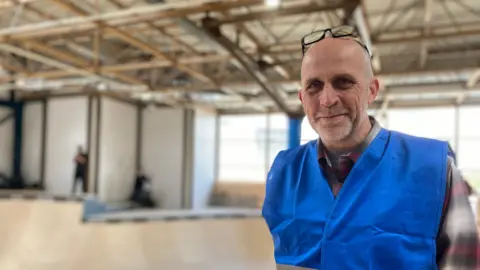 A man in a blue high viz jacket stood inside the skatepark