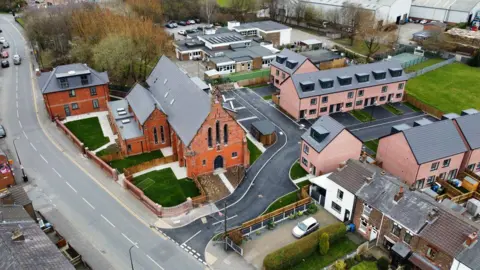 Prima An aerial view of the new-build St William's development in Wigan. The houses are a pinkish brick, built on a cul-de-sac, with St William's Church to the left-hand side.