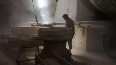 Reuters A person works at a ceramic tile production line at a factory in Gujarat's Morbi on 5 March 2026. He is surrounded by machines and pipes.