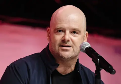 Getty Images Dan Houser speaks during In Conversation with Dan Houser: Grand Theft Auto, Red Dead Redemption, and now American Caper at 2025 Los Angeles Comic Con at Los Angeles Convention Center on September 27, 2025 in Los Angeles, California.