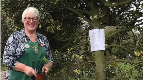 Jennifer Hall  Jennifer Hall wearing a green apron is holding a plant pot 