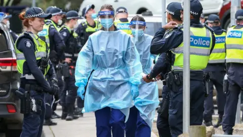 Getty Images Medical staff wearing protective equipment walk through a police guard