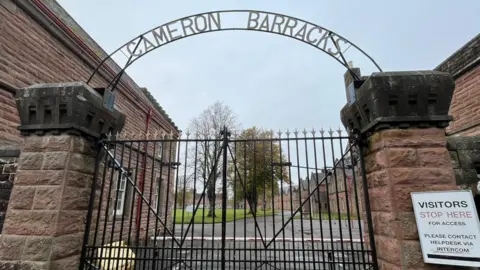 The entrance to Cameron Barracks with its metal gates and arched metal sign with the words "Cameron Barracks".