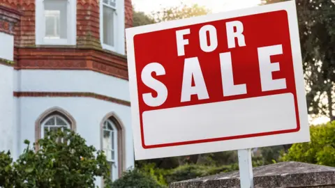 Getty Images A red sign with white writing saying "for sale" stands outside a townhouse