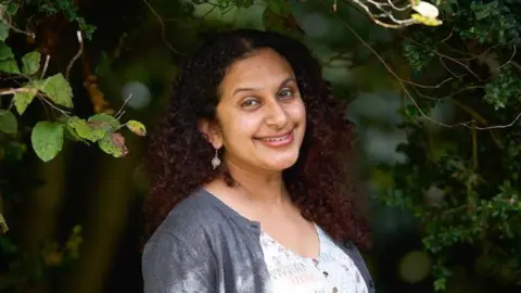 Simon Richardson Krishna smiling at the camera, behind her are some trees.