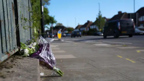 PA Media A single bouquet of flowers sitting against a fence on a path next to where the crash happened.