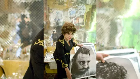 A woman with curly dark stands next to a large black and white phot of Castro's face